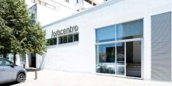 Front view of the Ferticentro fertility clinic in Coimbra with white facade, side tree, parked car and large glass entrance displaying the clinic logo