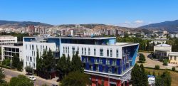 Aerial view of LeaderMed Clinic building in Tbilisi, Georgia surrounded by modern cityscape, palm trees and Caucasus mountains. Leading IVF fertility treatment center in prestigious location.